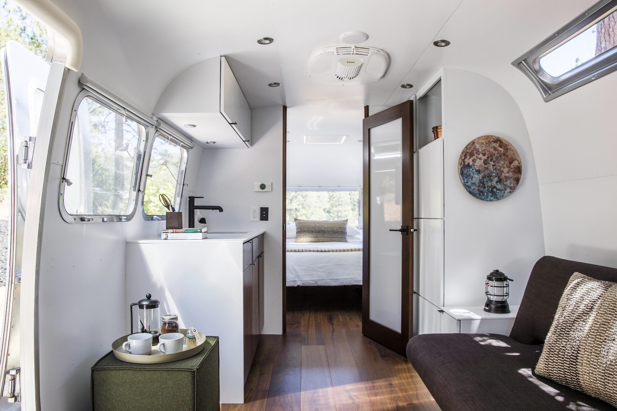 Inside Airstream suite. Features wide angle view of living area with futon couch, kitchenette, and doorway to bedroom at far end.