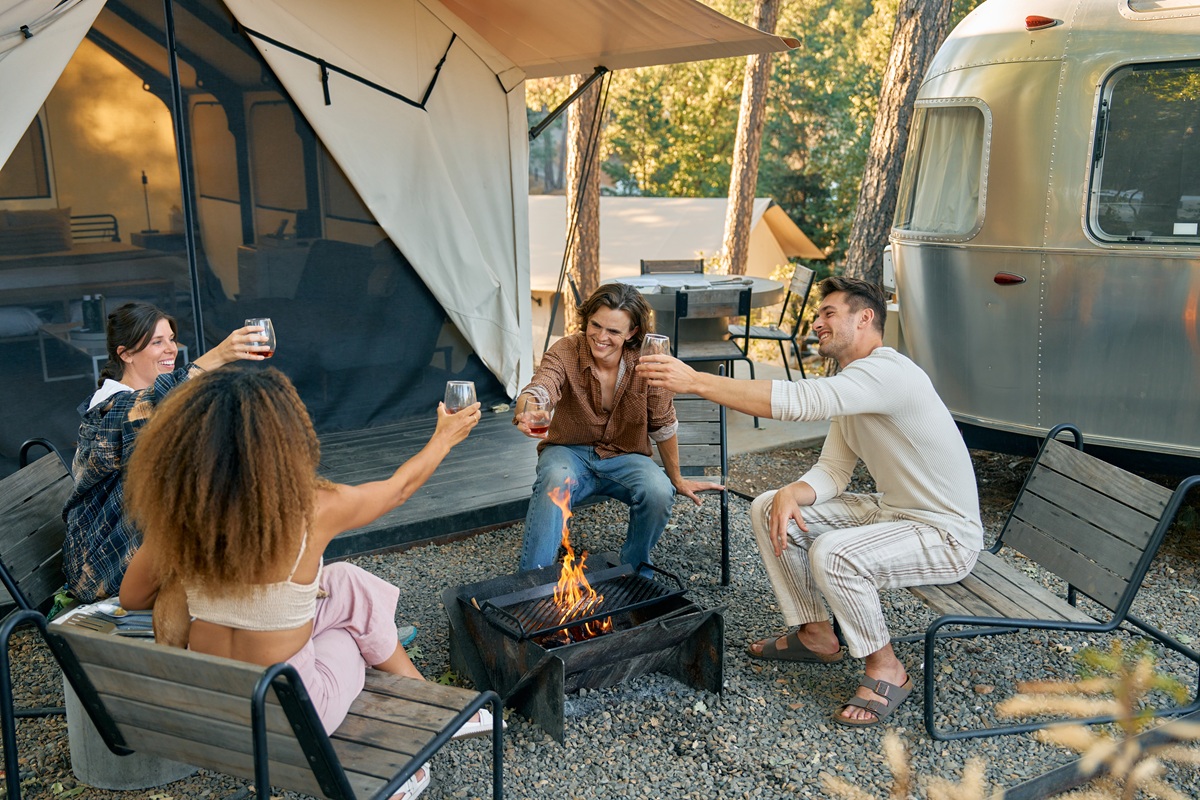 Friends by the fire in a BaseCamp suite comprised of a tent and Airstream accommodations combined in one site