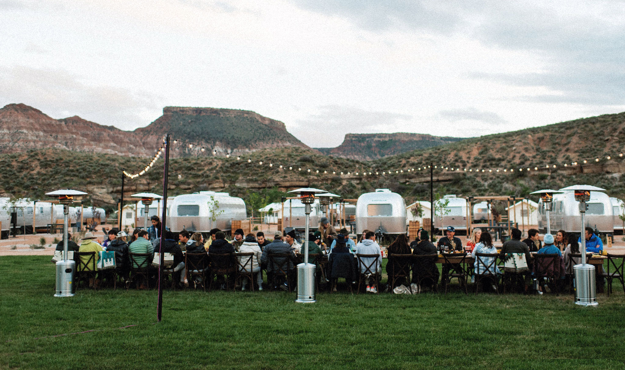 People dining outdoor in front of airstreams with lights and heaters