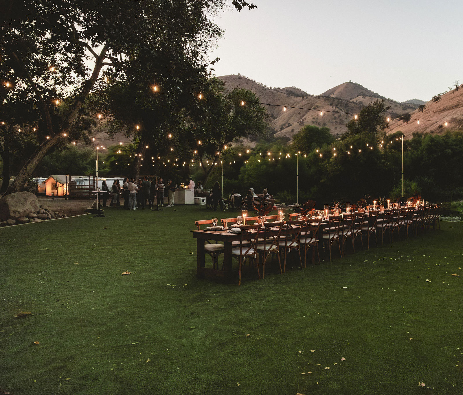 Group meeting in an outdoor area with table set up with candles. Trees and golden hills in the background at AutoCamp Sequoia. Known as Ponderosa Lawn.