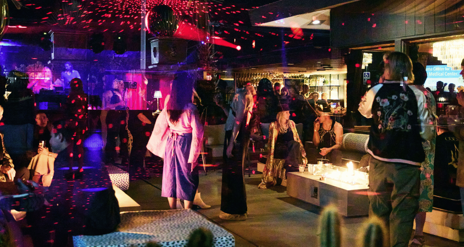 Group of people in a bar with a disco ball reflecting pink light across the room
