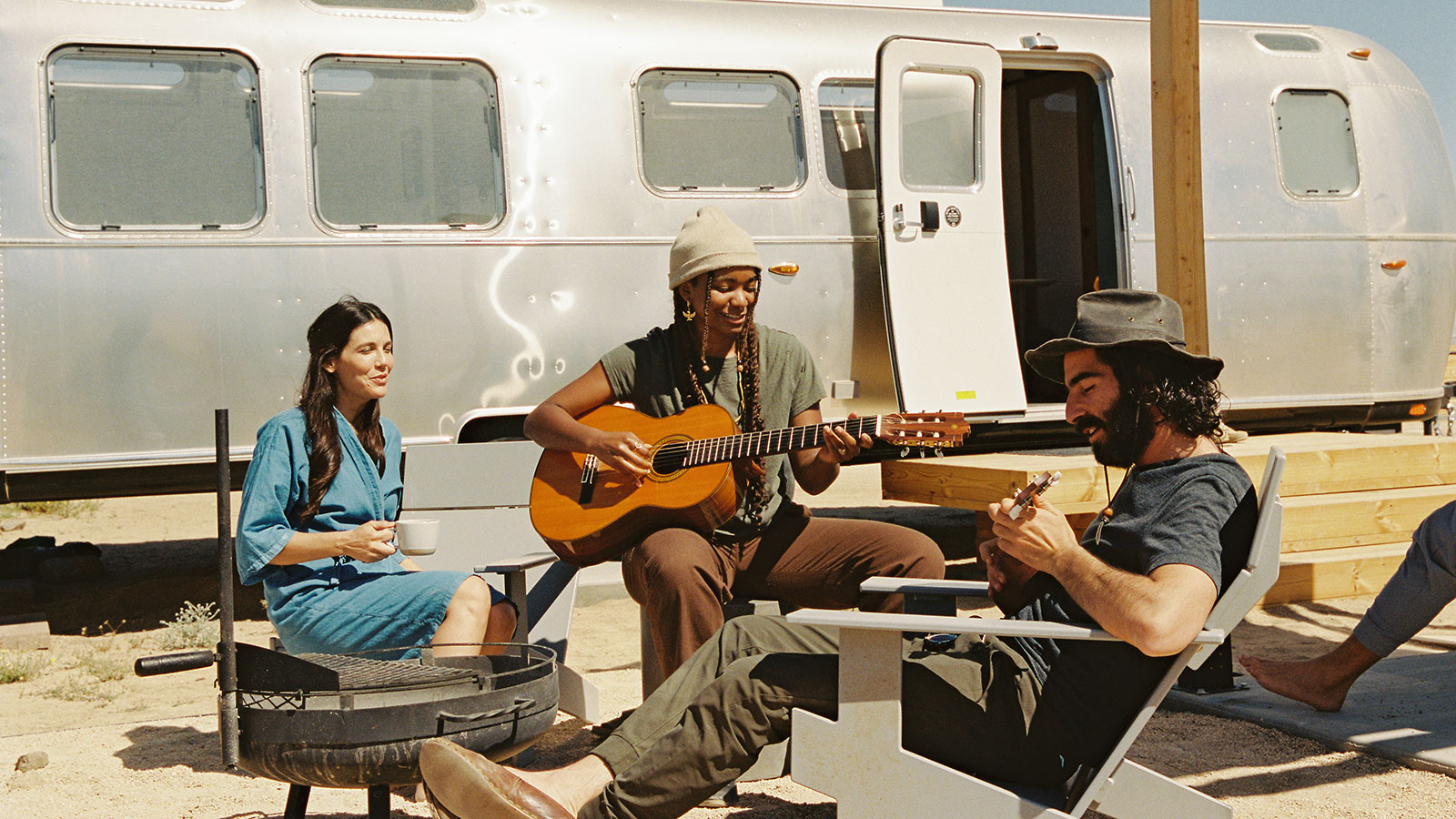 Friends playing guitar and drinking coffee in front of an Airstream