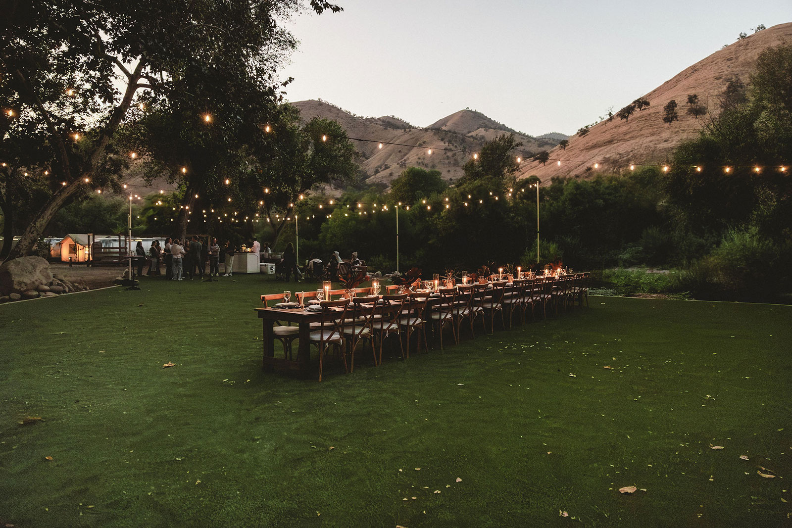 Group meeting in an outdoor area with table set up with candles. Trees and golden hills in the background at AutoCamp Sequoia. Known as Ponderosa Lawn.