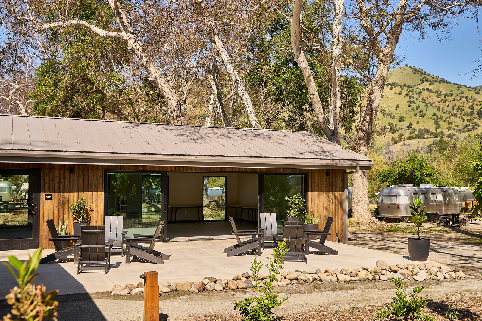 Group meeting in an outdoor patio area with lounge chairs set up. Trees and golden hills in the background at AutoCamp Sequoia.