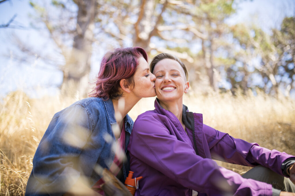 Two women outside, one giving a kiss on the cheek to the other smiling